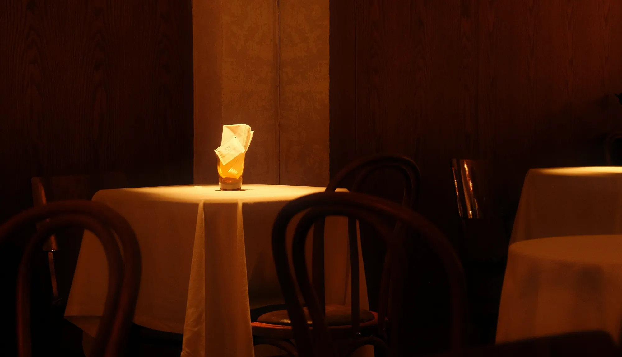 A single candle on a white tablecloth in a dim dining room