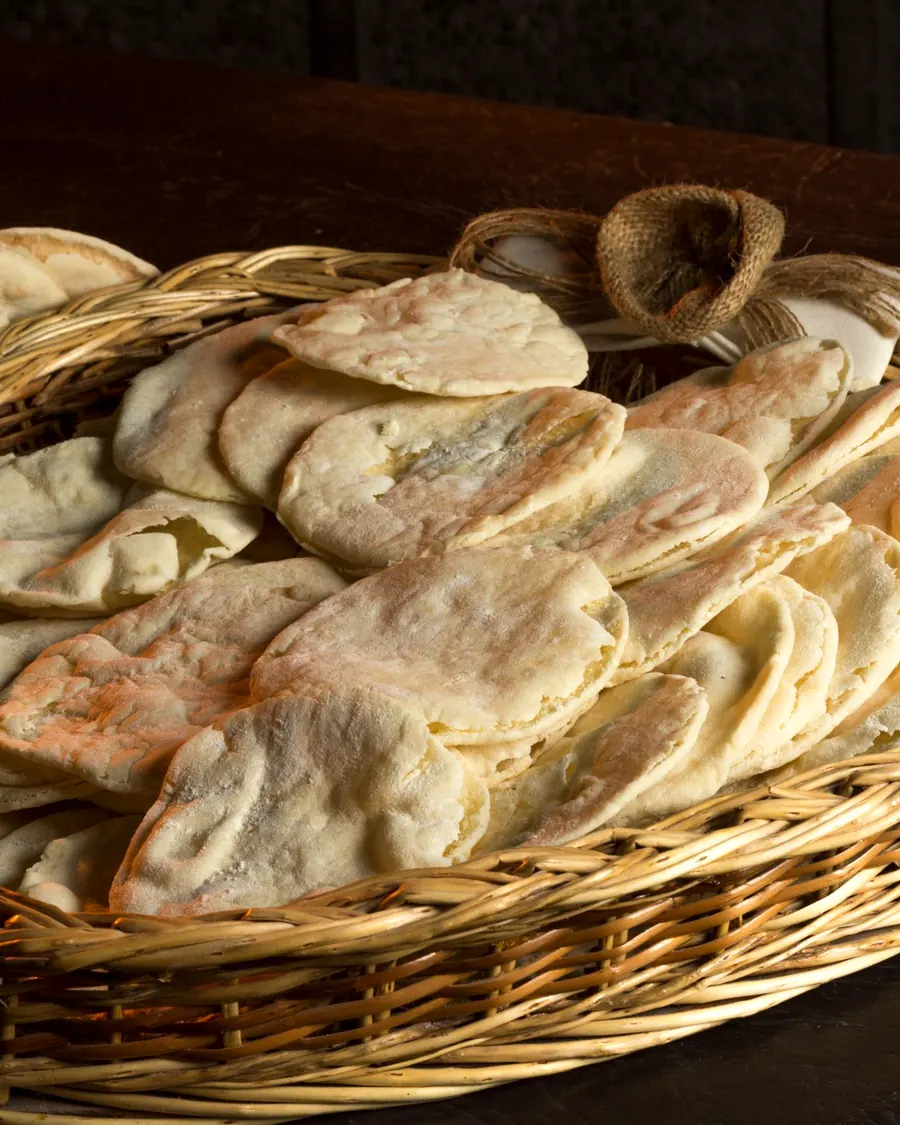 A basket of warm pita bread on a wooden table