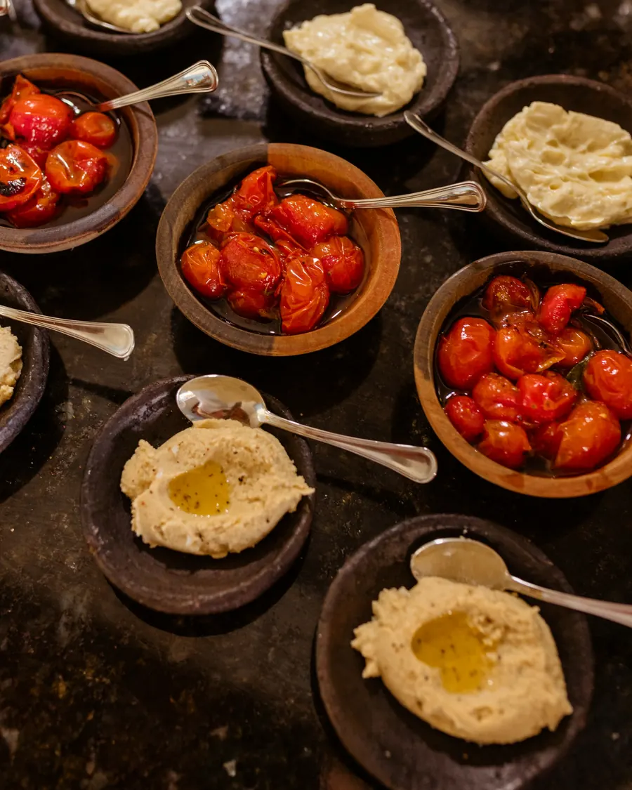 Clay bowls of hummus, garlic dip and roasted cherry tomatoes