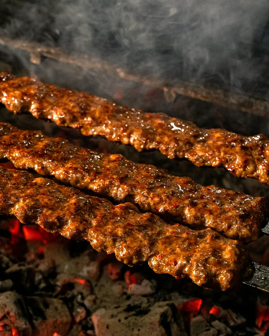 Three lamb kofta skewers grilling over glowing charcoal
