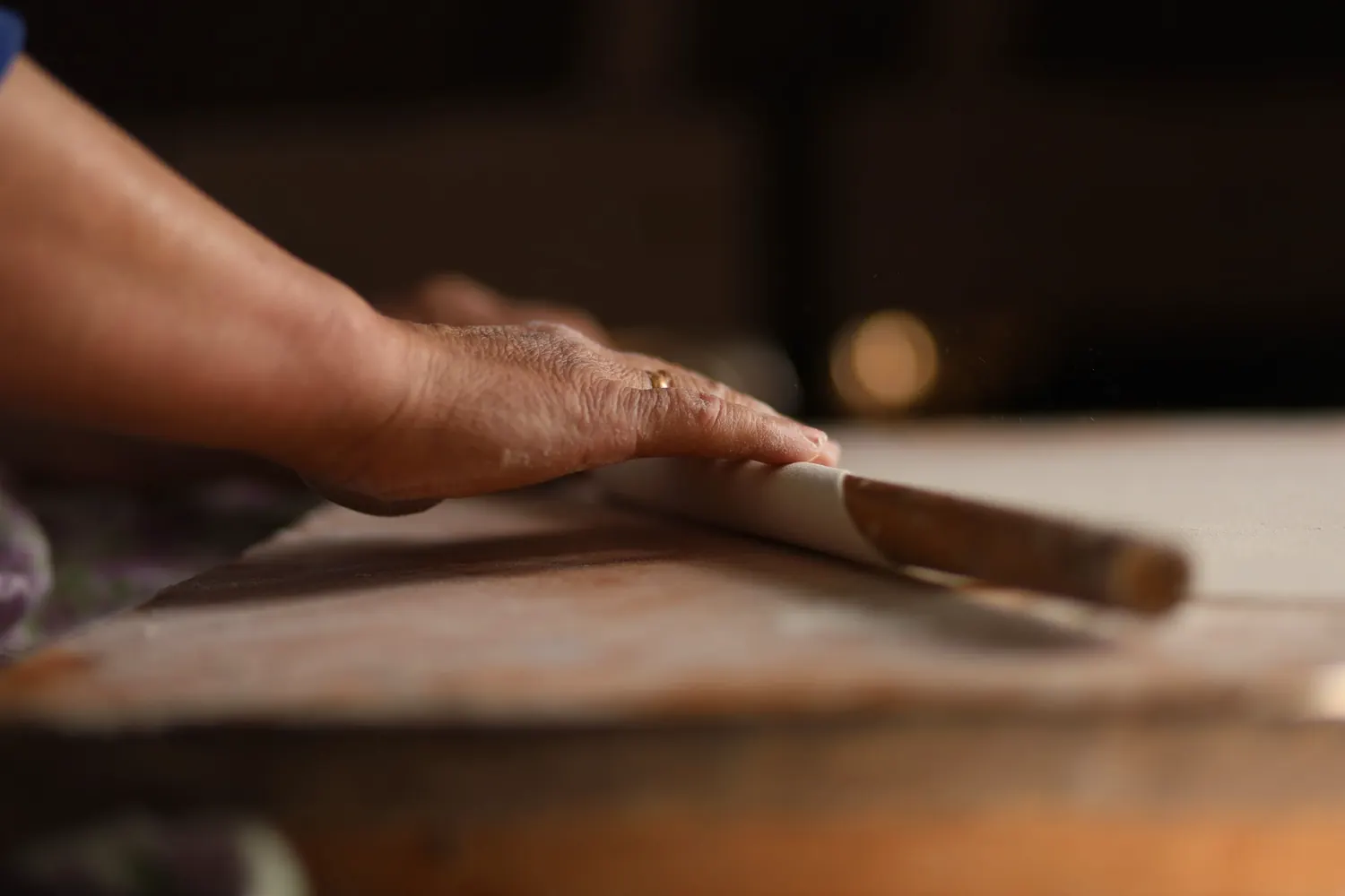 An older woman’s hands rolling out dough with a wooden pin
